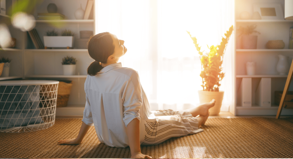 Mujer sentada en el suelo respirando tranquila frente a la luz del sol