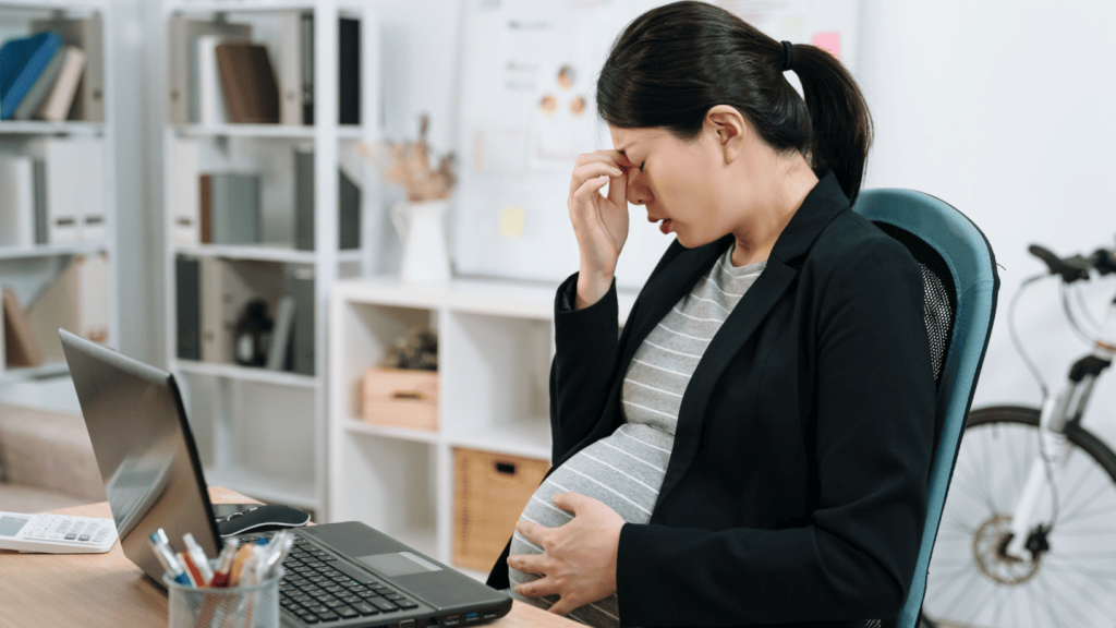 Mujer embarazada con estrés en el trabajo, llevándose la mano a la frente mientras sostiene su vientre